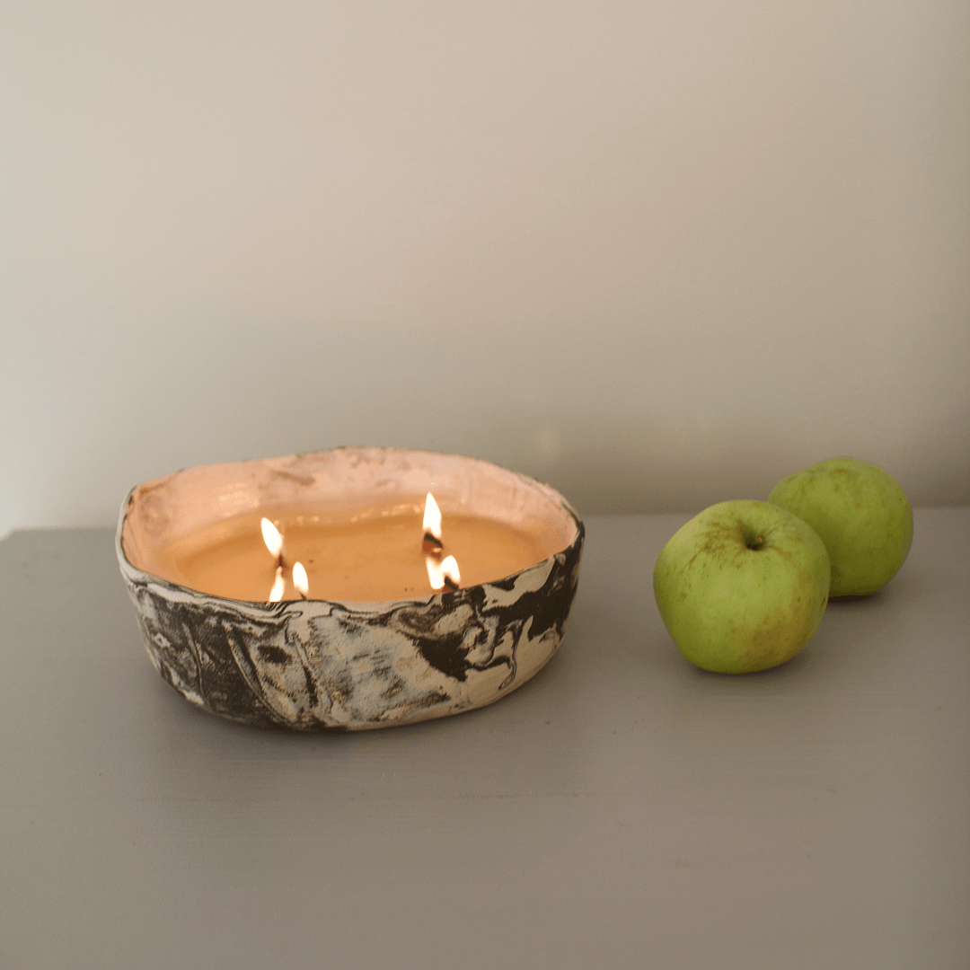 Ceramic bowl with a candle and two green apples on a gray surface