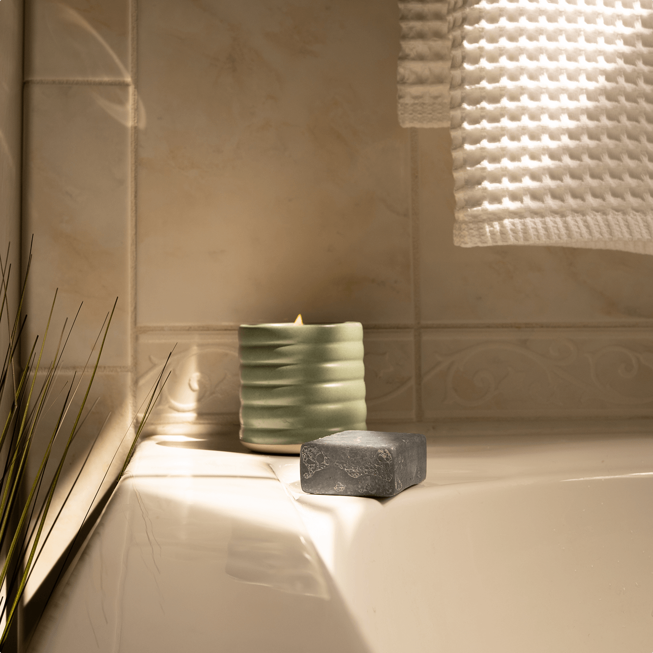 Clean Candle and soap on a bathtub ledge with tiled wall in the background