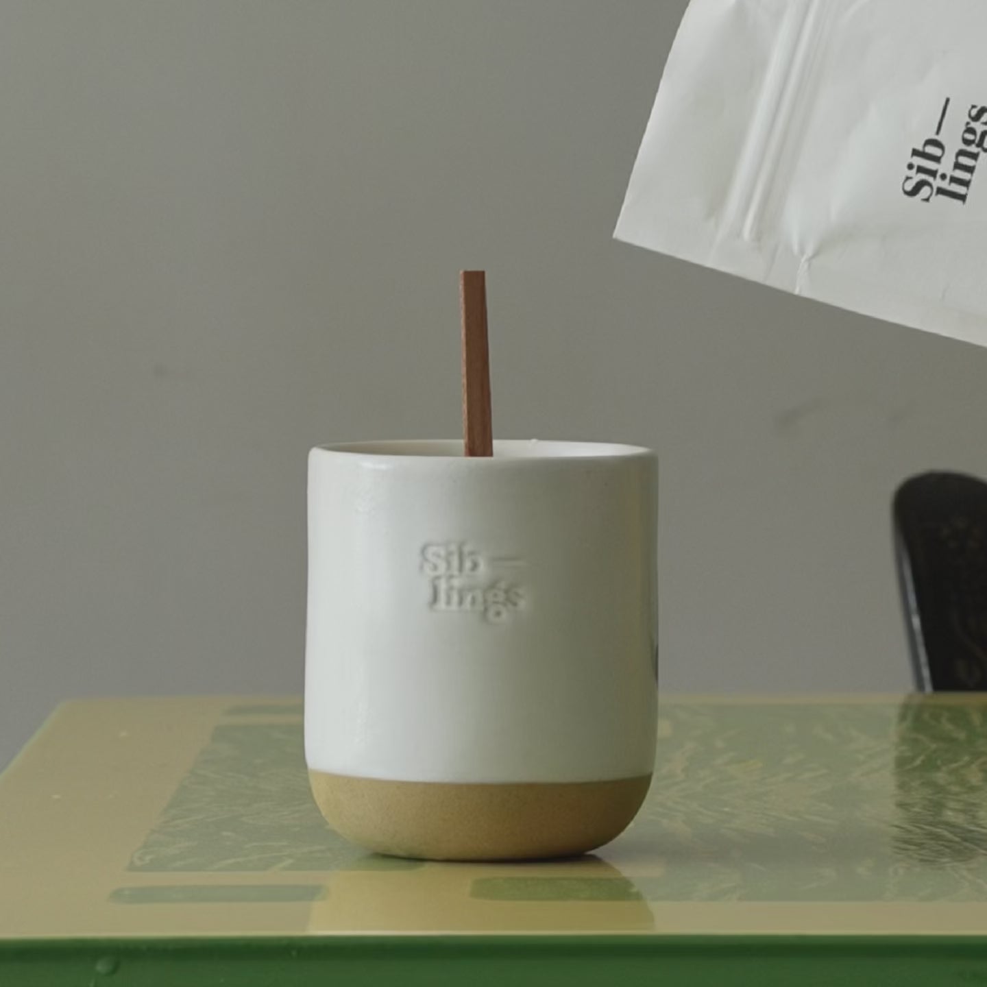 Demonstrating the refill process: pouring melted wax from a Siblings bag into a white cloud vessel with a wooden wick, accompanied by the text 'Melt, Pour, Enjoy'.